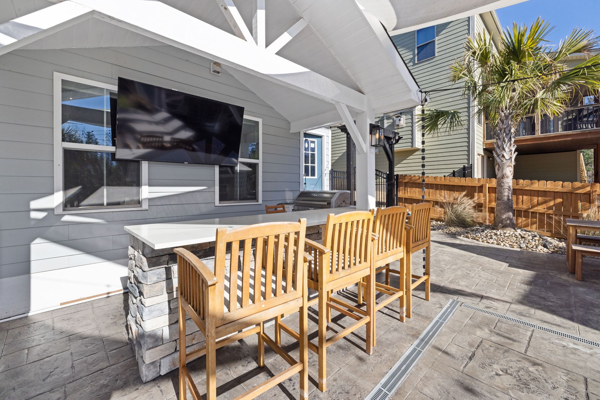 Spacious patio featuring wooden seating, stone bar, and wall-mounted TV under a covered area.